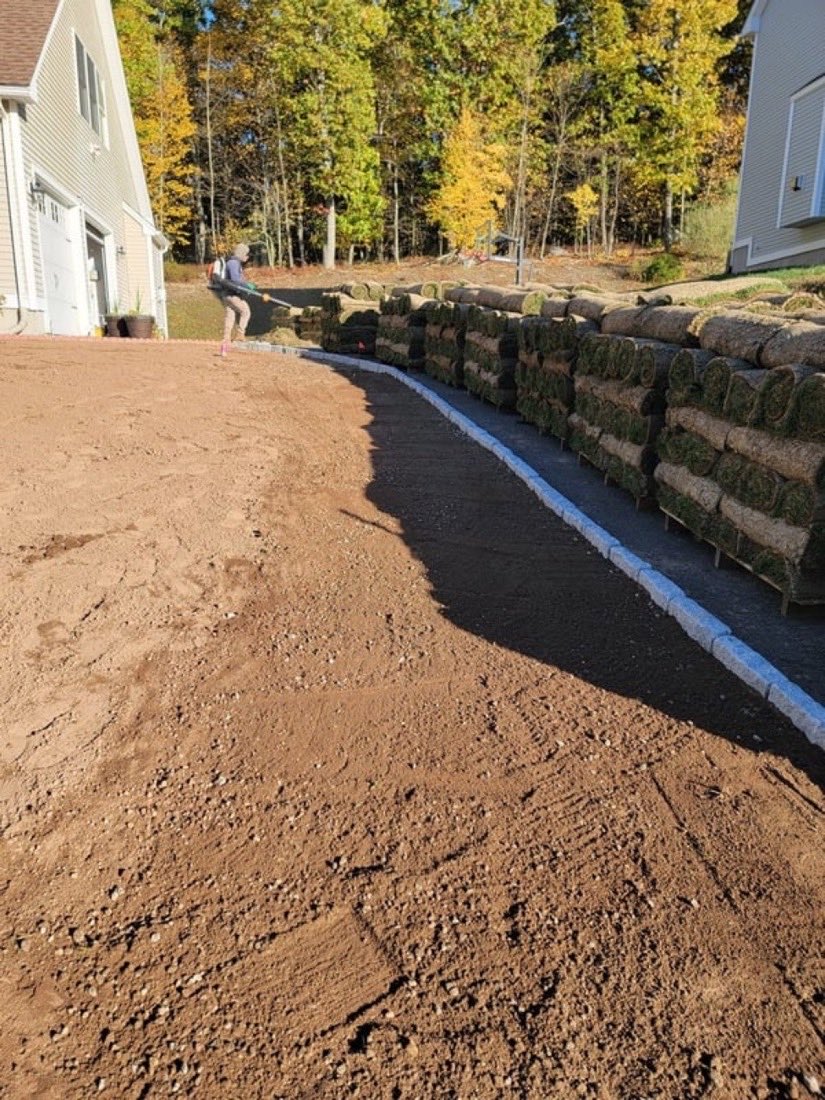 A curved stone retaining wall with rolls of sod stacked along it, ready to lay.